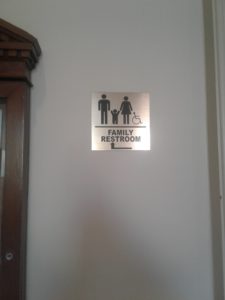 small brass plaque reading 'Family restroom' with an arrow to the left. Top half dominated by adult and child figures with a small child-sized wheelchair symbol