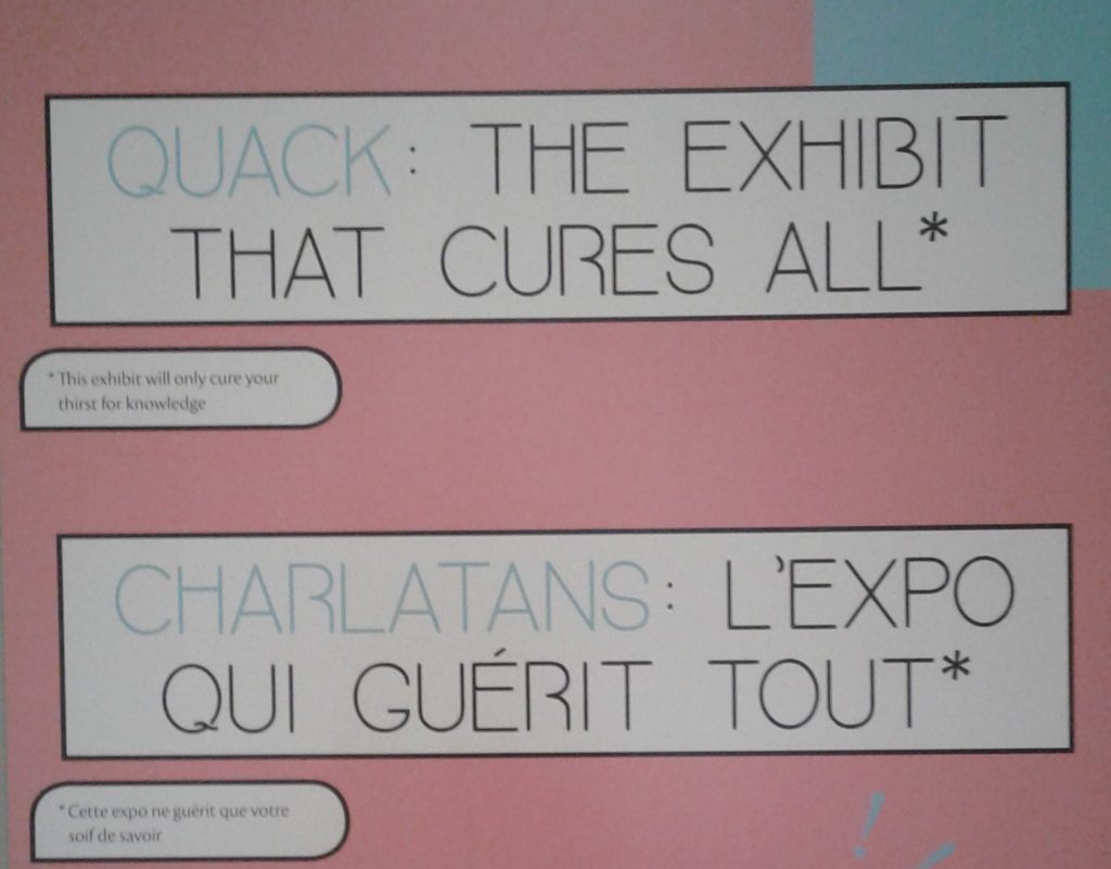 Pink exhibition text from the Museum of Health Care, title reads "Quack: The Exhibition that Cures All*" in English and French. In small text under the title reads "*This exhibition will only cure your thirst for knowledge"